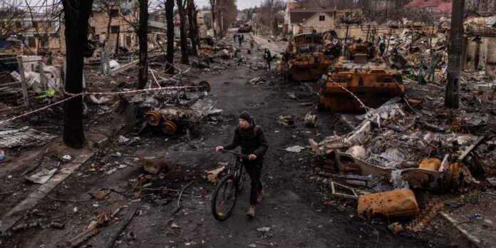 A man pushes his bike through debris and destroyed Russian military vehicles on a street on April 06, 2022 in Bucha, Ukraine. Hundreds of bodies were found in the days after Ukrainian forces regained control of the town.