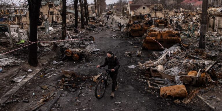 A man pushes his bike through debris and destroyed Russian military vehicles on a street on April 06, 2022 in Bucha, Ukraine. Hundreds of bodies were found in the days after Ukrainian forces regained control of the town.